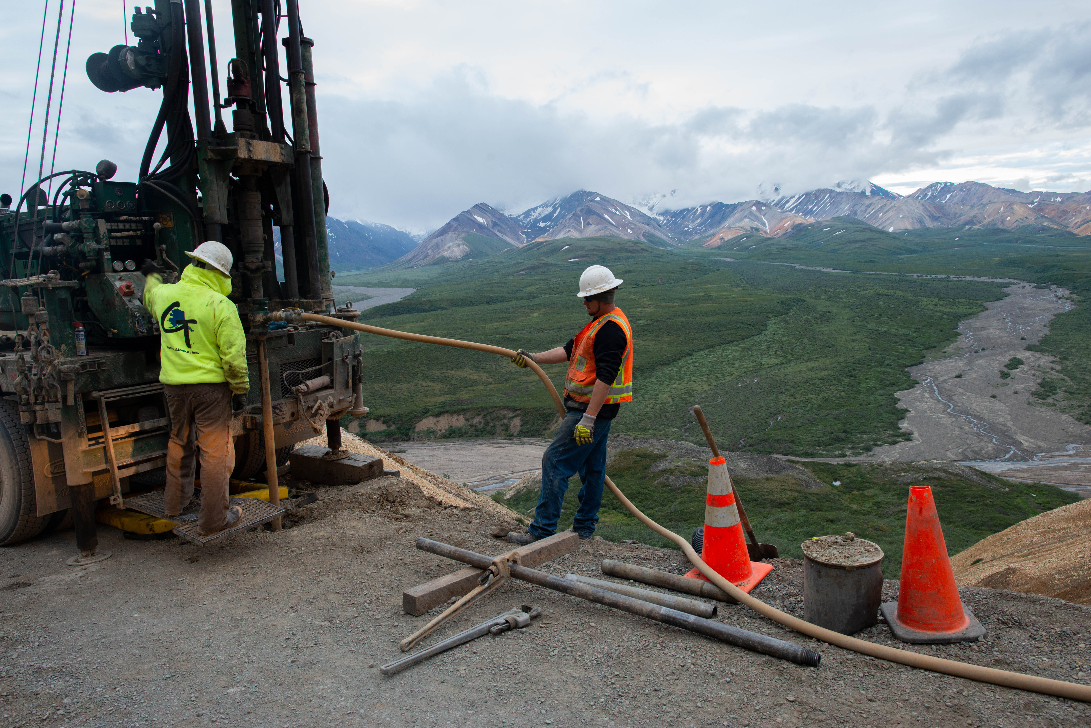 two men on a mountainside next to a drill rig