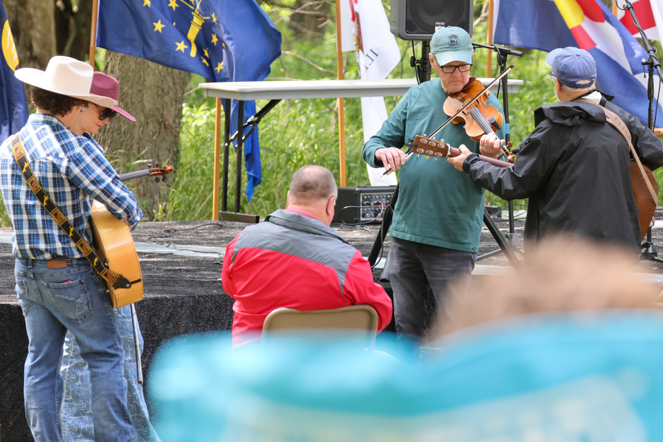 Five individuals stand around playing stringed instruments in front of a stage.
