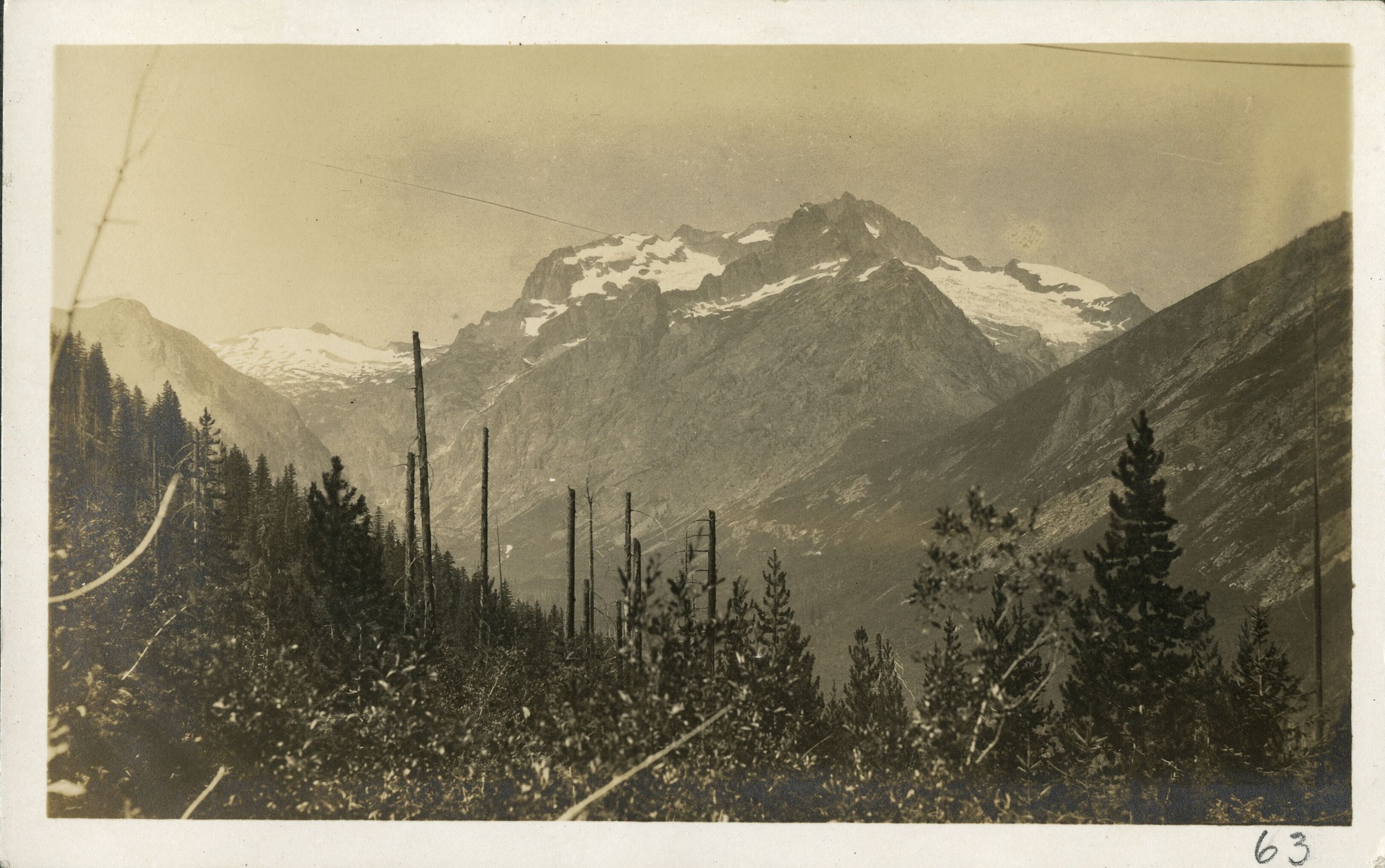 A mountain lake in the foreground, fire scarred hill mid-field, and a mountain with glacier in background.