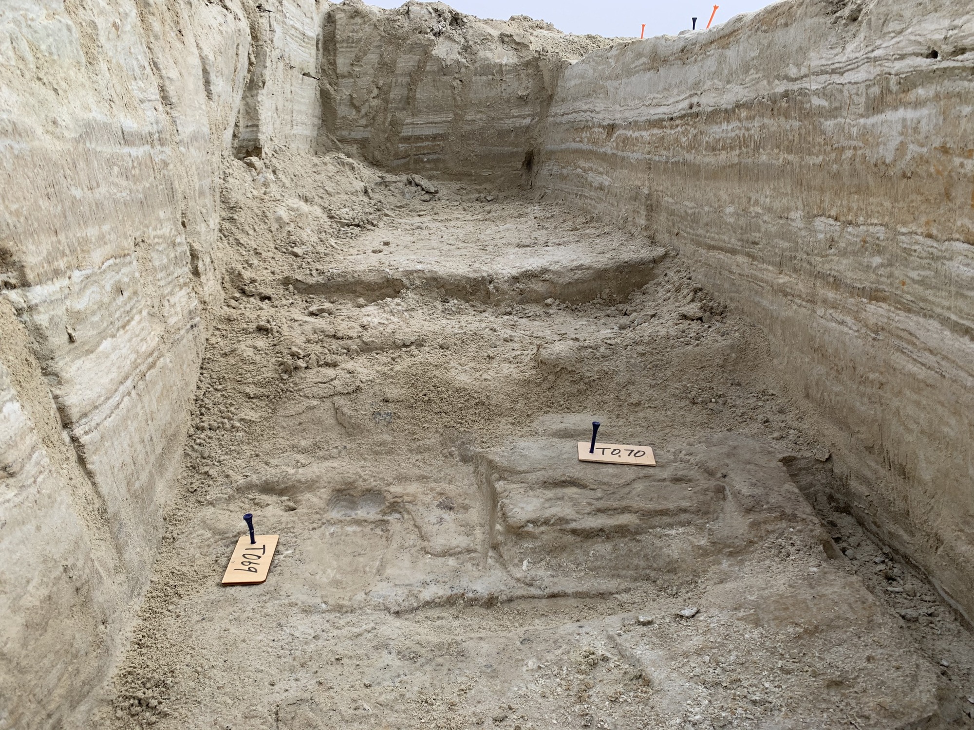 A close-up view of human footprints at the base of a dug-out trench. Four footprints are marked as T064, T067, T066, and T002.