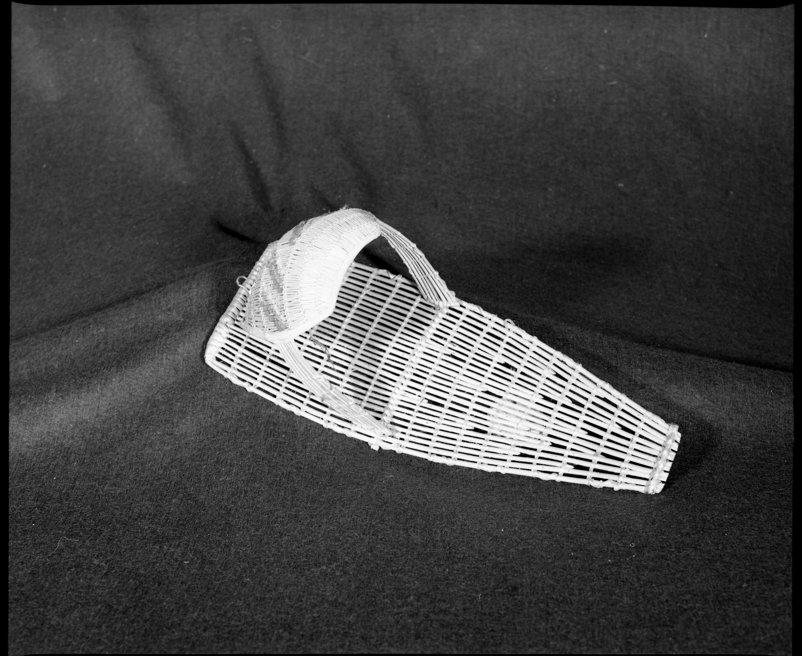 Marie Rozier Collection, Catalog No. 39. Object: Model Washoe cradlebasket. Dimensions: 16 x 6". Materials: Willow, cotton cloth. Technology: Plain twined backboard, diagonally twined hood, down to right slant of turns. Collection History: Purchased at Woodford's Store, ca. 1950, by Marie Rozier, same day as No. 56, for $1.10. Photographed by Michael Dixon, December 1982. Catalogued by Craig Bates and Barbara Beroza. Yosemite Collections, National Park Service.