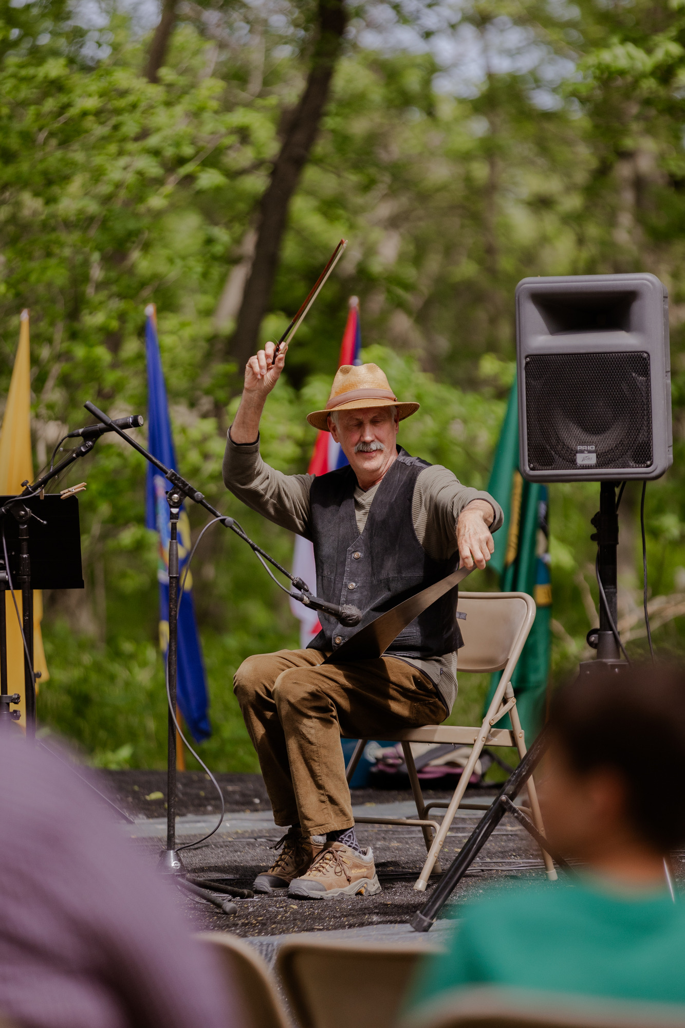 Man with straw hat appears to play music on a large hand saw using a bow usually reserved for a fiddle.