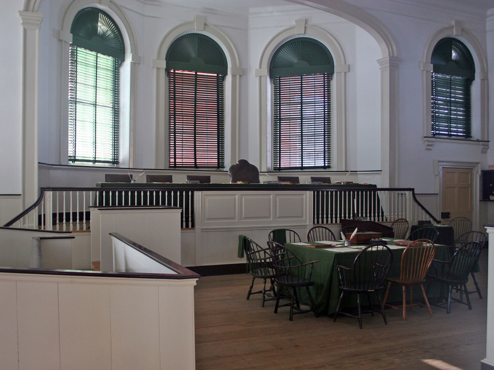Color photo of a courtroom with a raised judge's bench with six chairs, a jury box, and one table covered with a green cloth.
