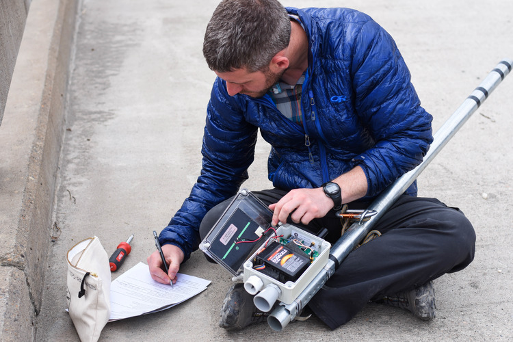 a man with an electronic device and a notebook sitting on the ground