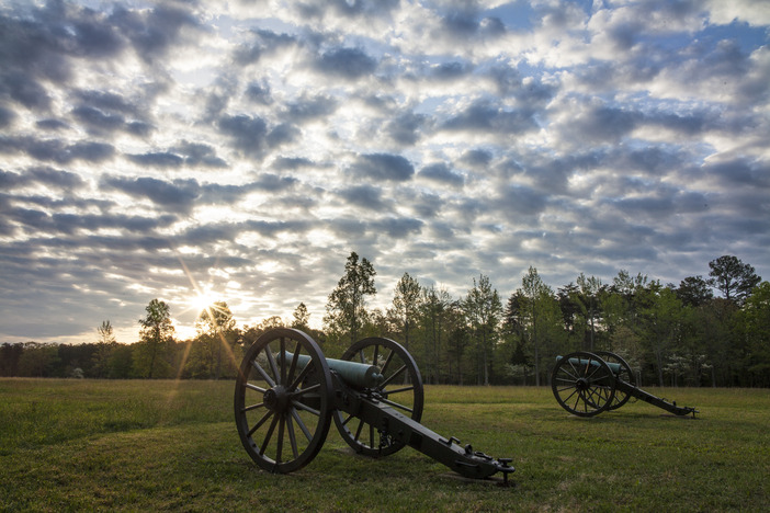 Two cannons pointed at a field with a cloudy sky.