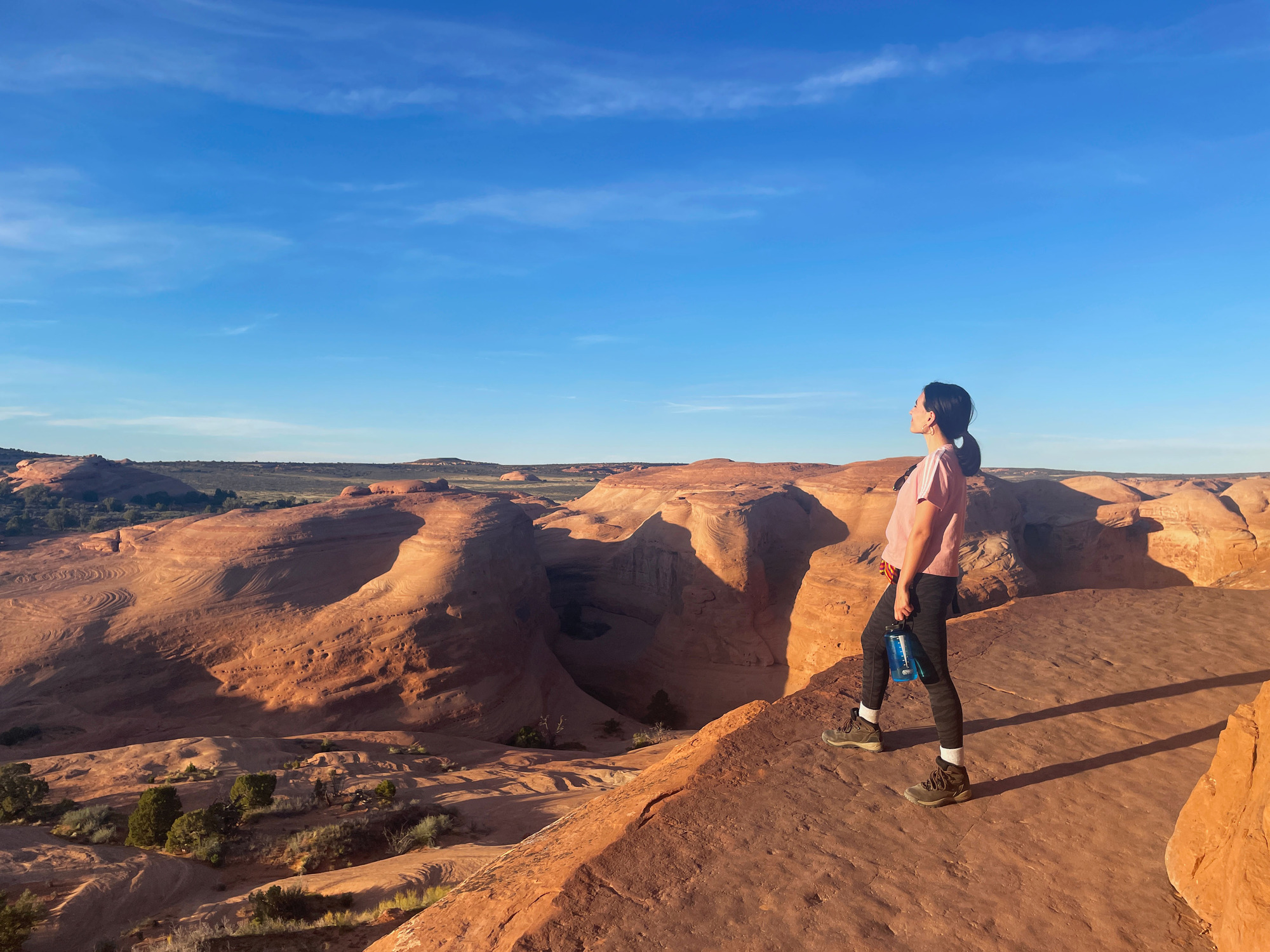 Woman standing on a narrow sandstone trail looking at the landscape of tall sandstone fins. 