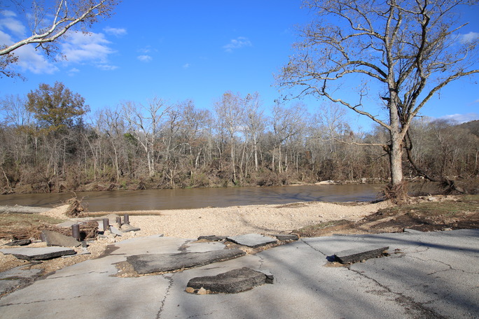 Asphalt, gravel, and trees are scattered across a paved ramp to the river. The ramp is torn apart.