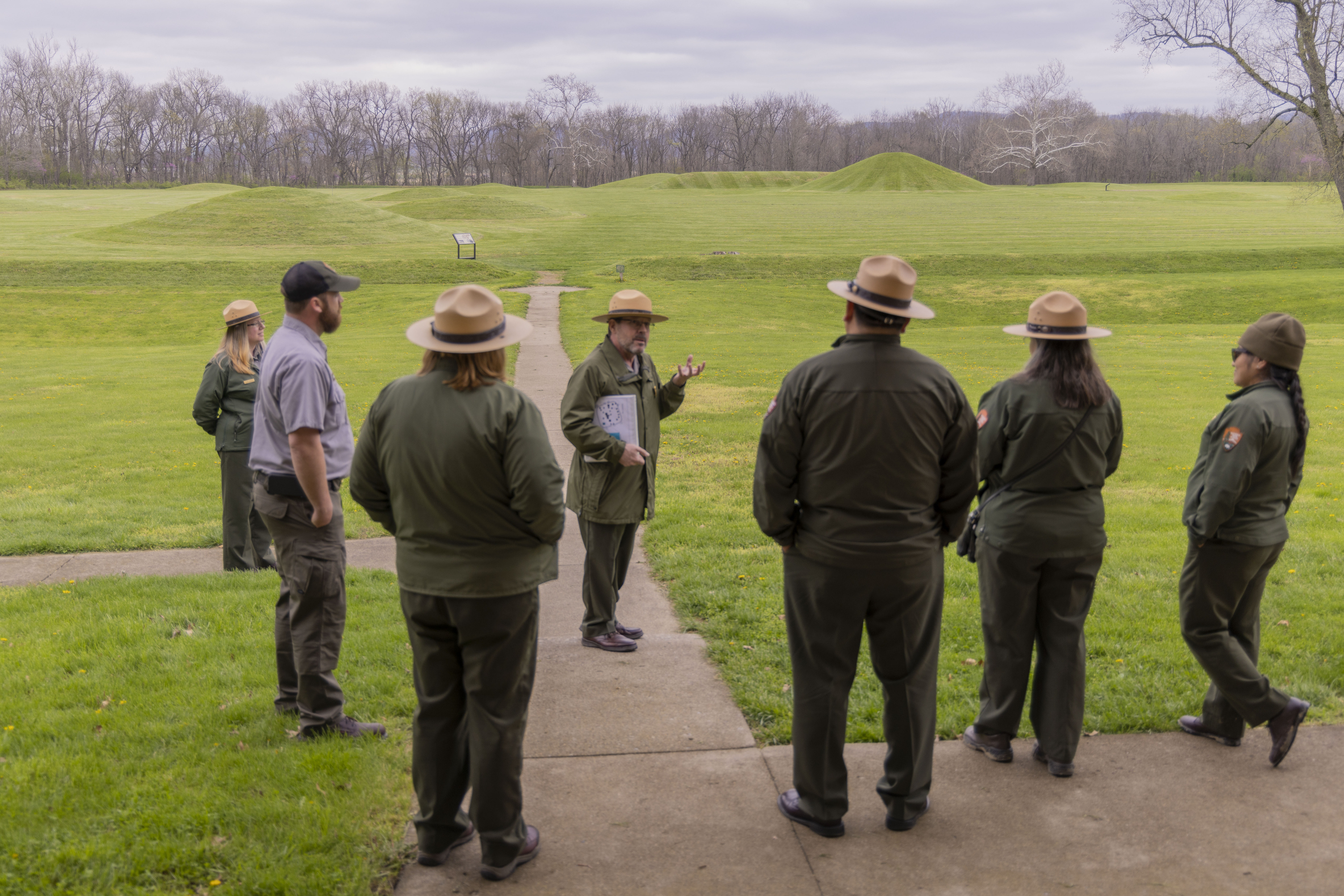 A man in a tan flat hat faces other rangers in flat hats as he speaks to them
