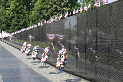 Flower wreaths stand in front of the black marble Vietnam Veterans Memorial. 