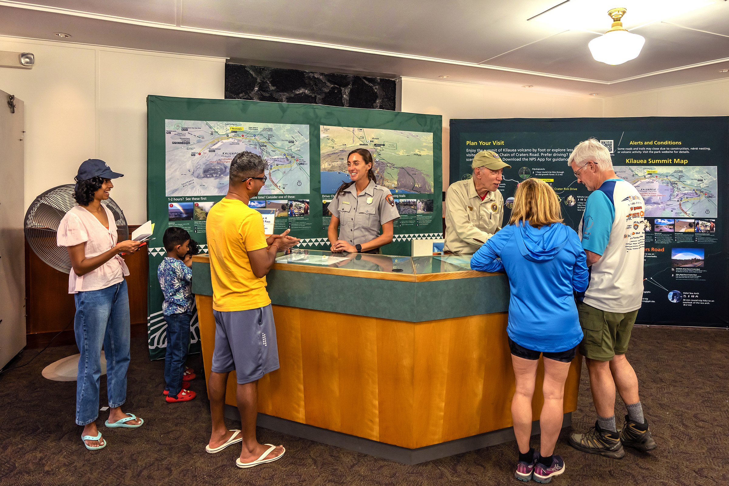 A Park Ranger and Park Volunteer stand behind a desk helping park visitors