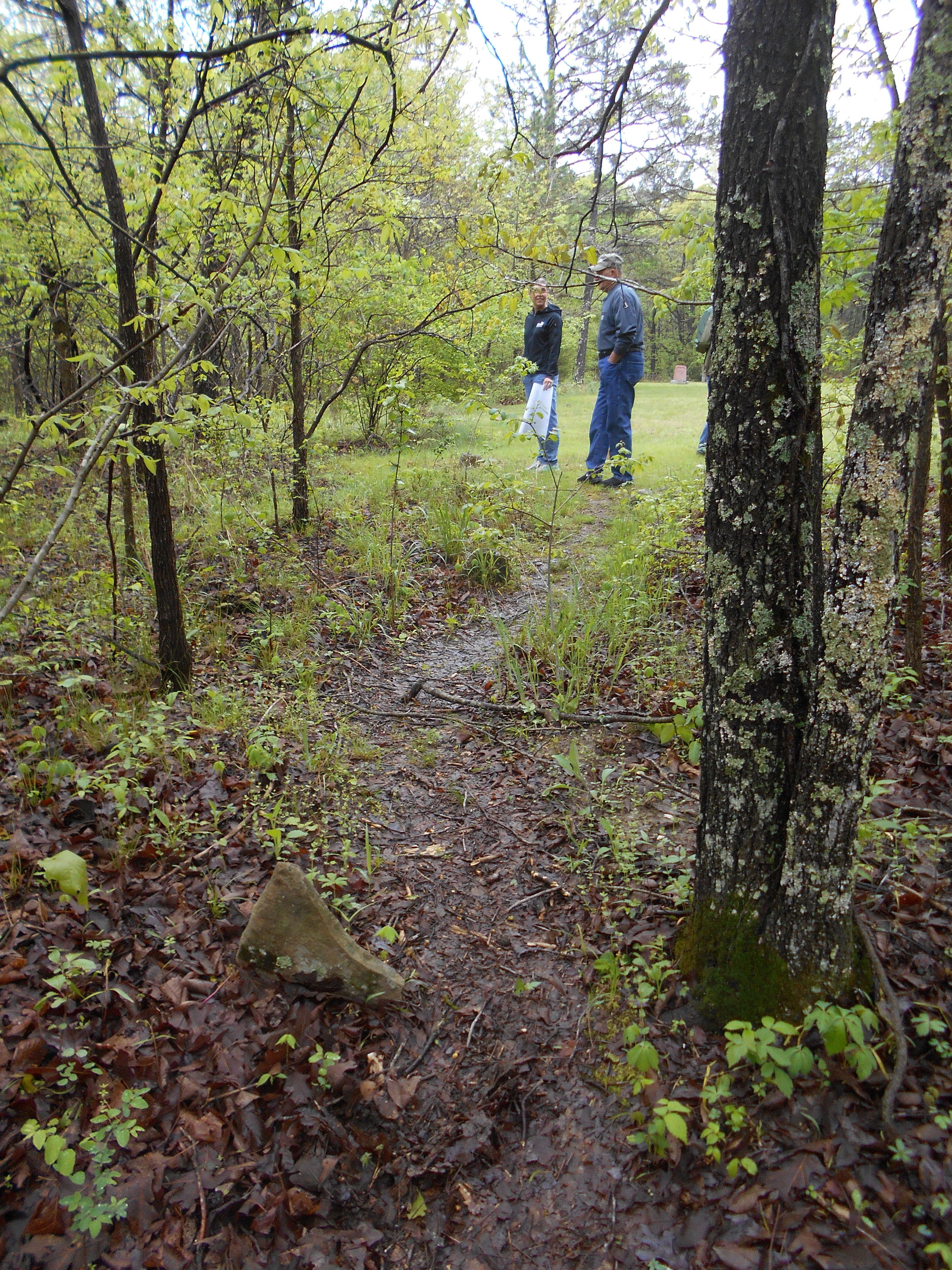 A group of people standing on a trail in a wooded area.