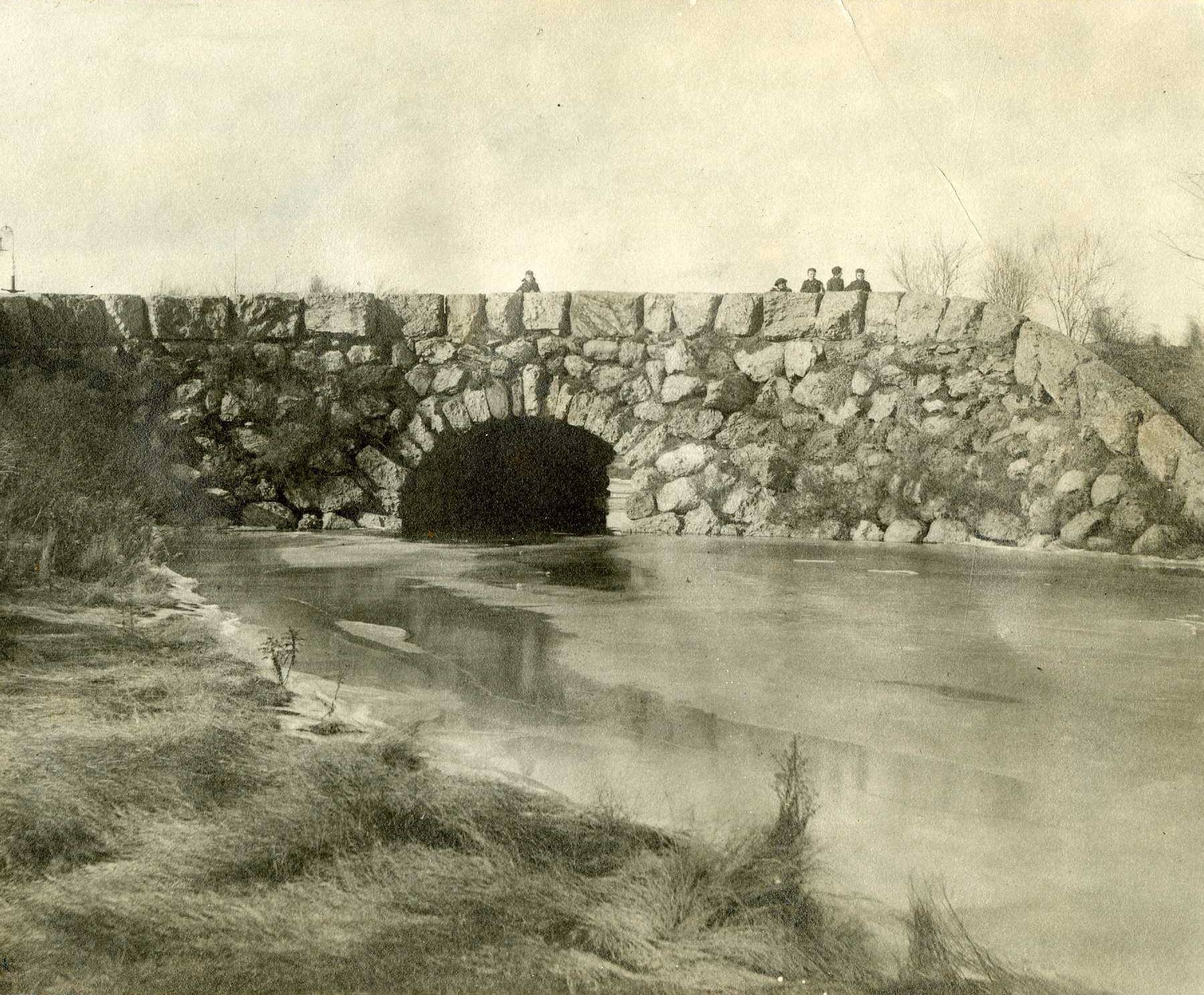 Black and white of stone bridge over water with people on top