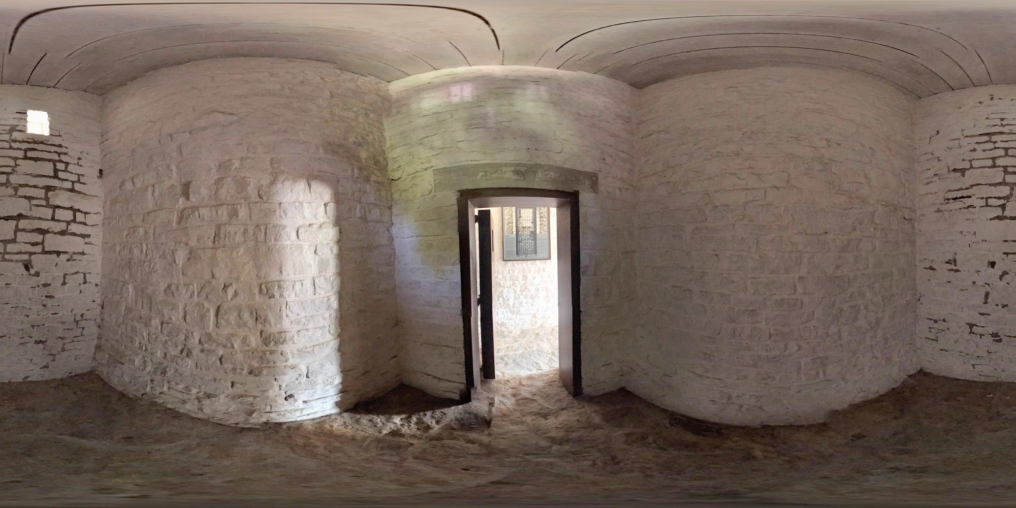 Small room with stone floor and walls with a door with bars on it.