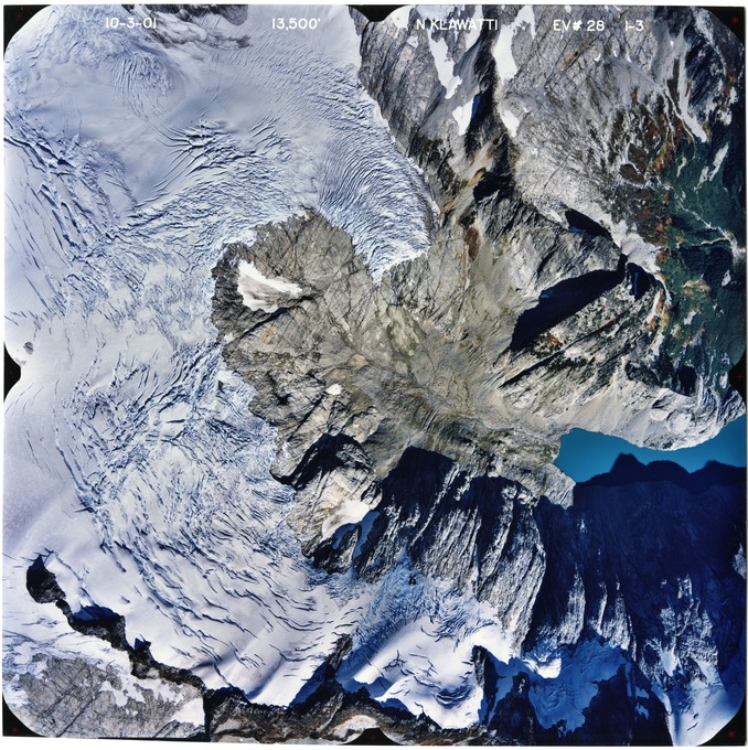 Color aerial photograph of glacier, snowfields, and alpine lake on mountain peak.
