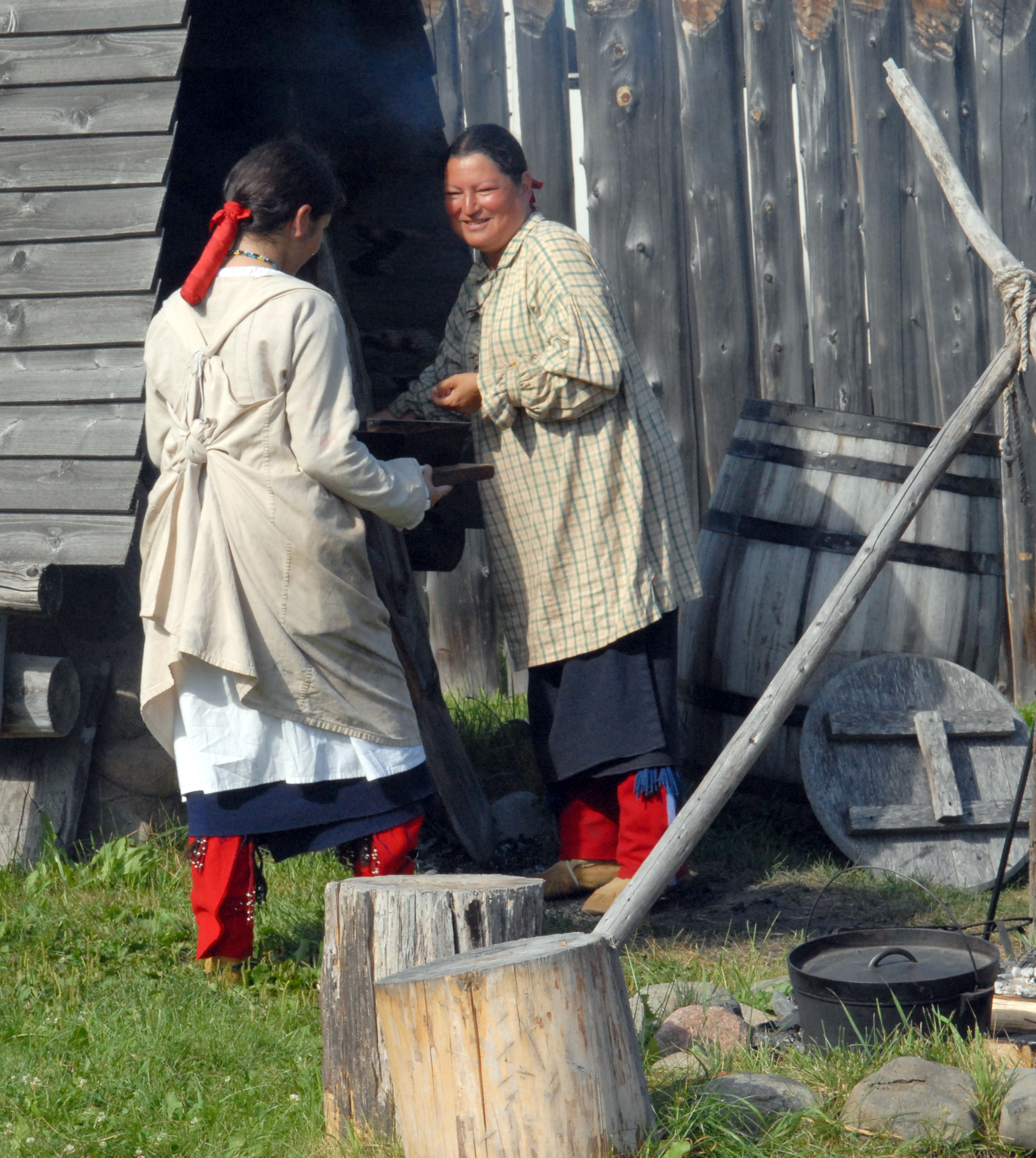 Two people in historic clothing removing a covered pan from a historic bread oven.