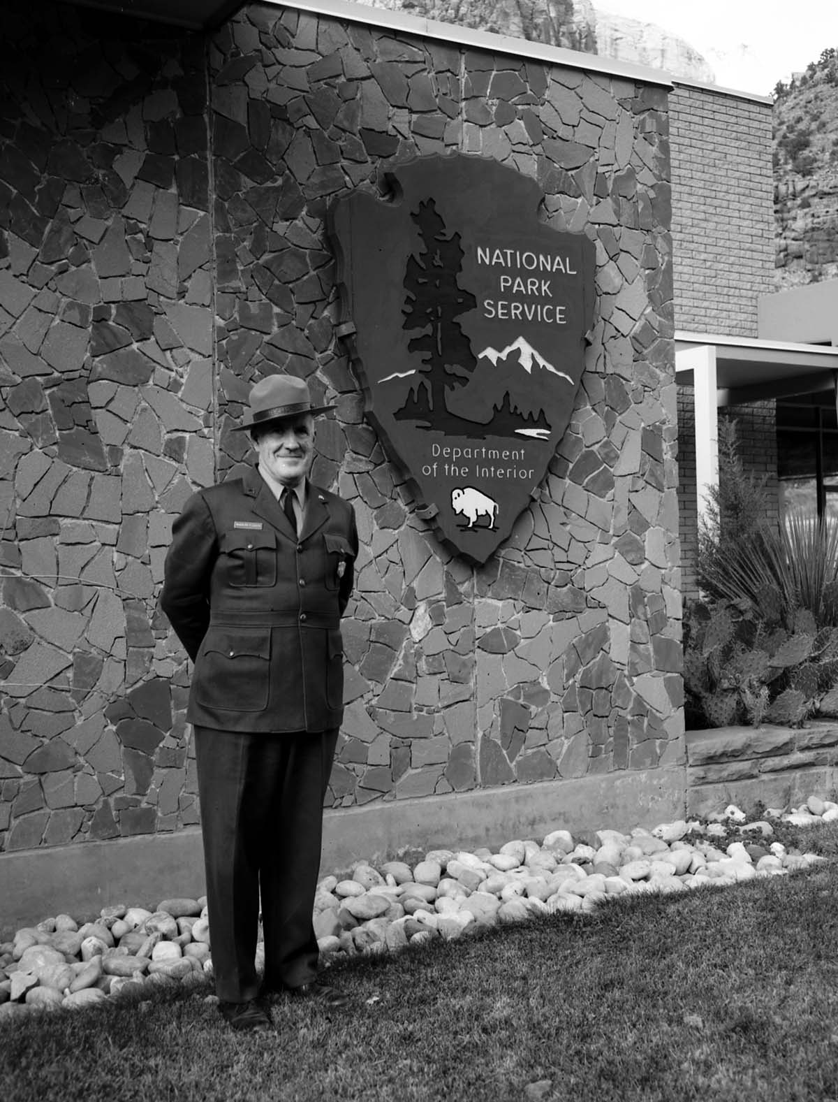 Rudy Lueck at time of retirement, next to NPS arrowhead outside Mission 66 Visitor Center and Museum and headquarters.