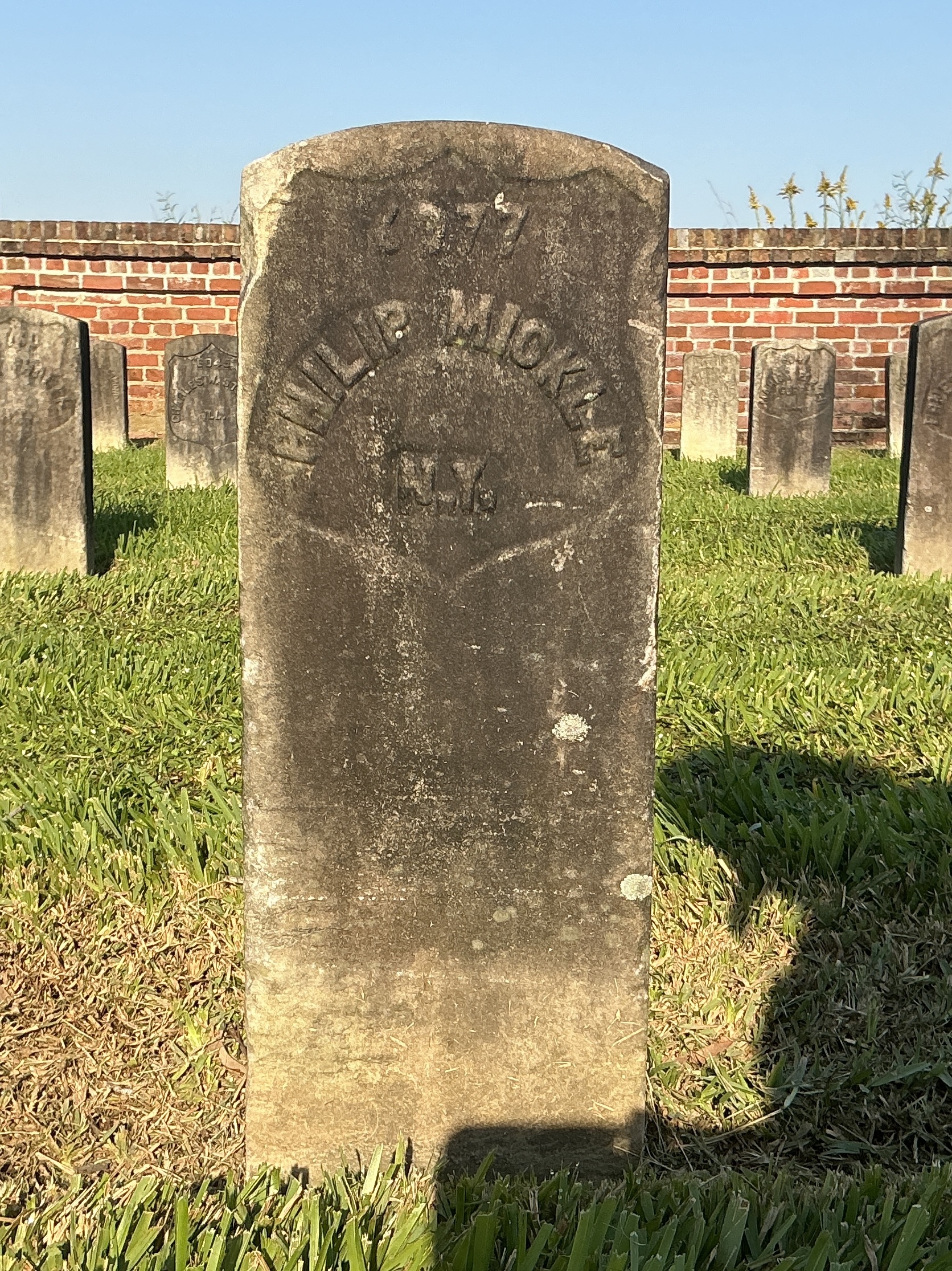Front of historic upright marble headstone with recessed shield with recessed lettering face.