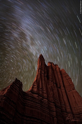 A time lapse photo of stars above a red sandstone spire. The movement of the stars around the north star makes each star look like a line.  