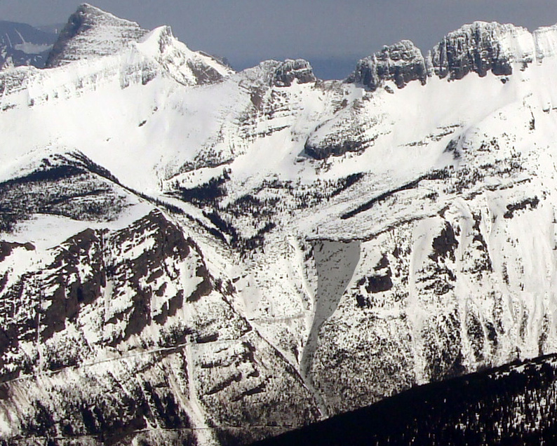 An avalanche path runs down a distant, snowy mountainside.