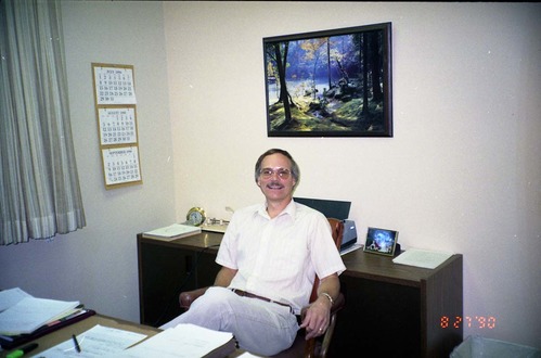 Color Photos of administration personnel. Man seated at desk.