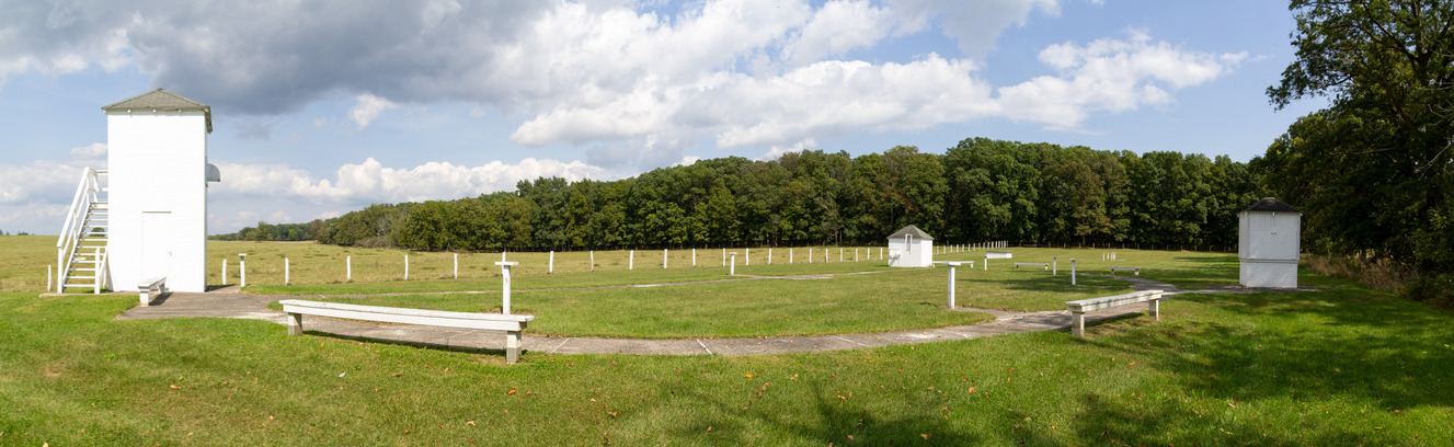 A tall rectangular white building in a mowed lawn and benches places on the outskirts.