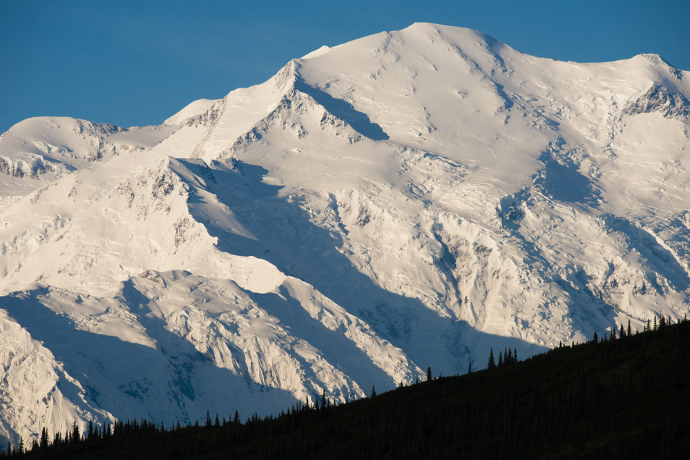A landscape of hills, forests and a huge, snowy mountain