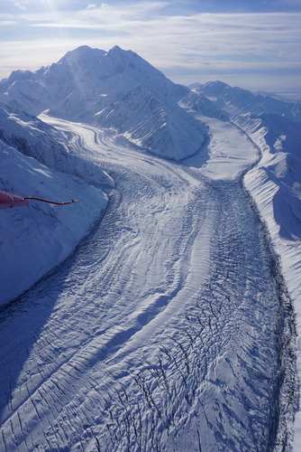 a huge snowy mountain with two branches of a large glacier flowing down. the two forks eventually meet and form one vast, long glacier heavily marked by crevasses