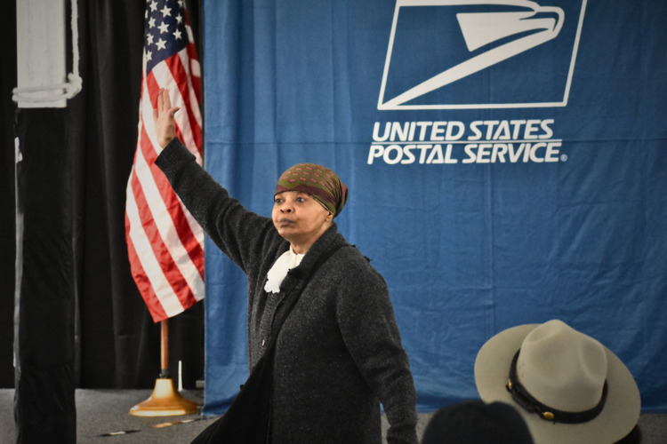 A woman dressed in historical clothing portrays Harriet Tubman to an audience.