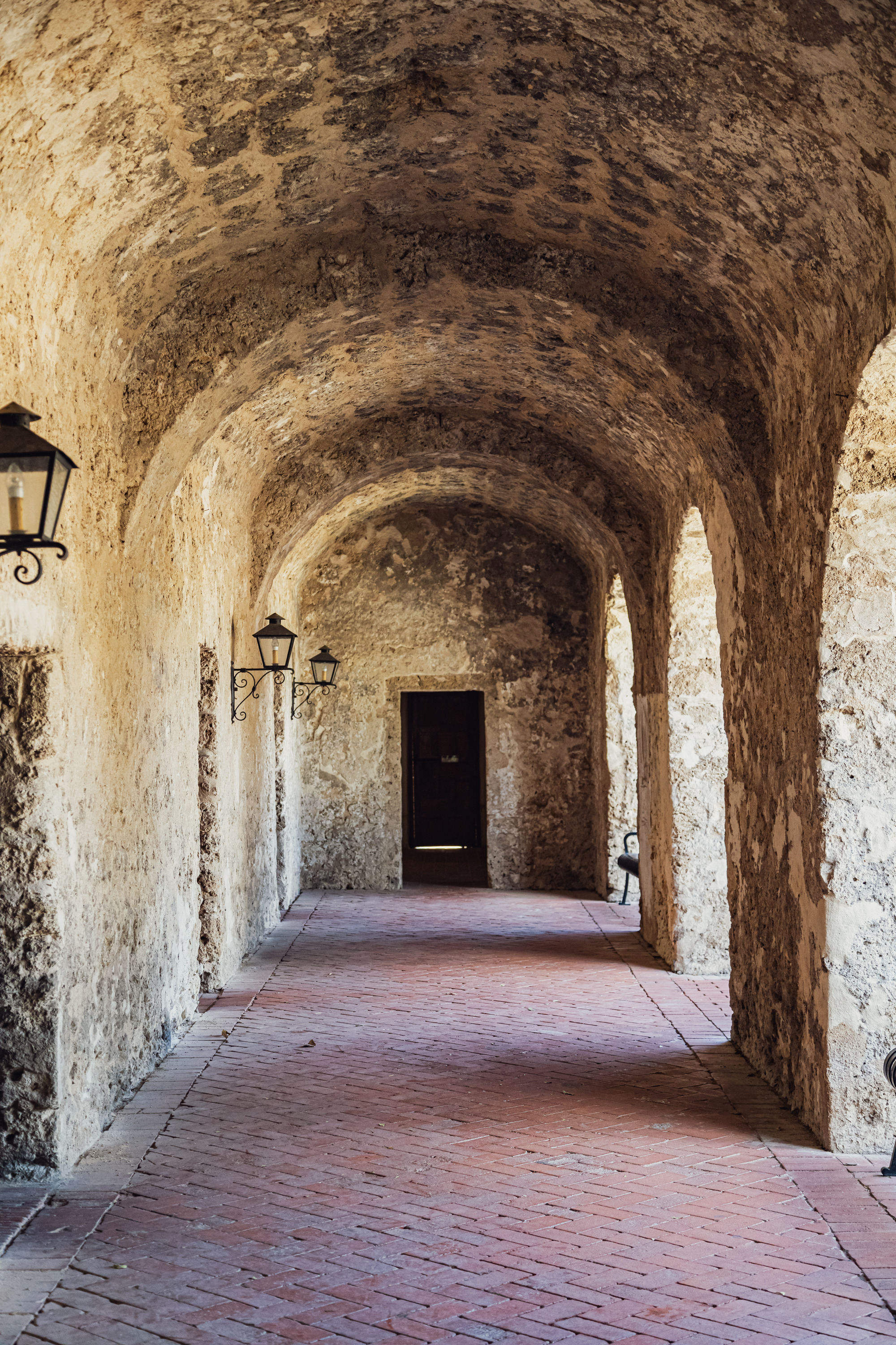 Convento archway with lamp posts and a door at the end of the hall. 