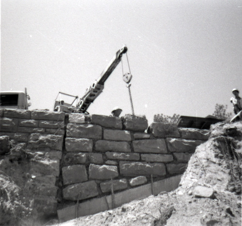 Men operating crane to place rocks for retaining wall along East Rim road during repairs.