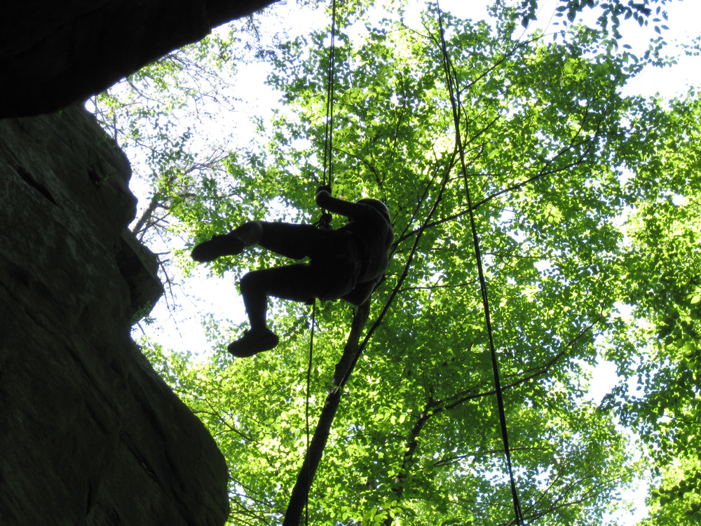 person hanging on a rope next to a cliff face