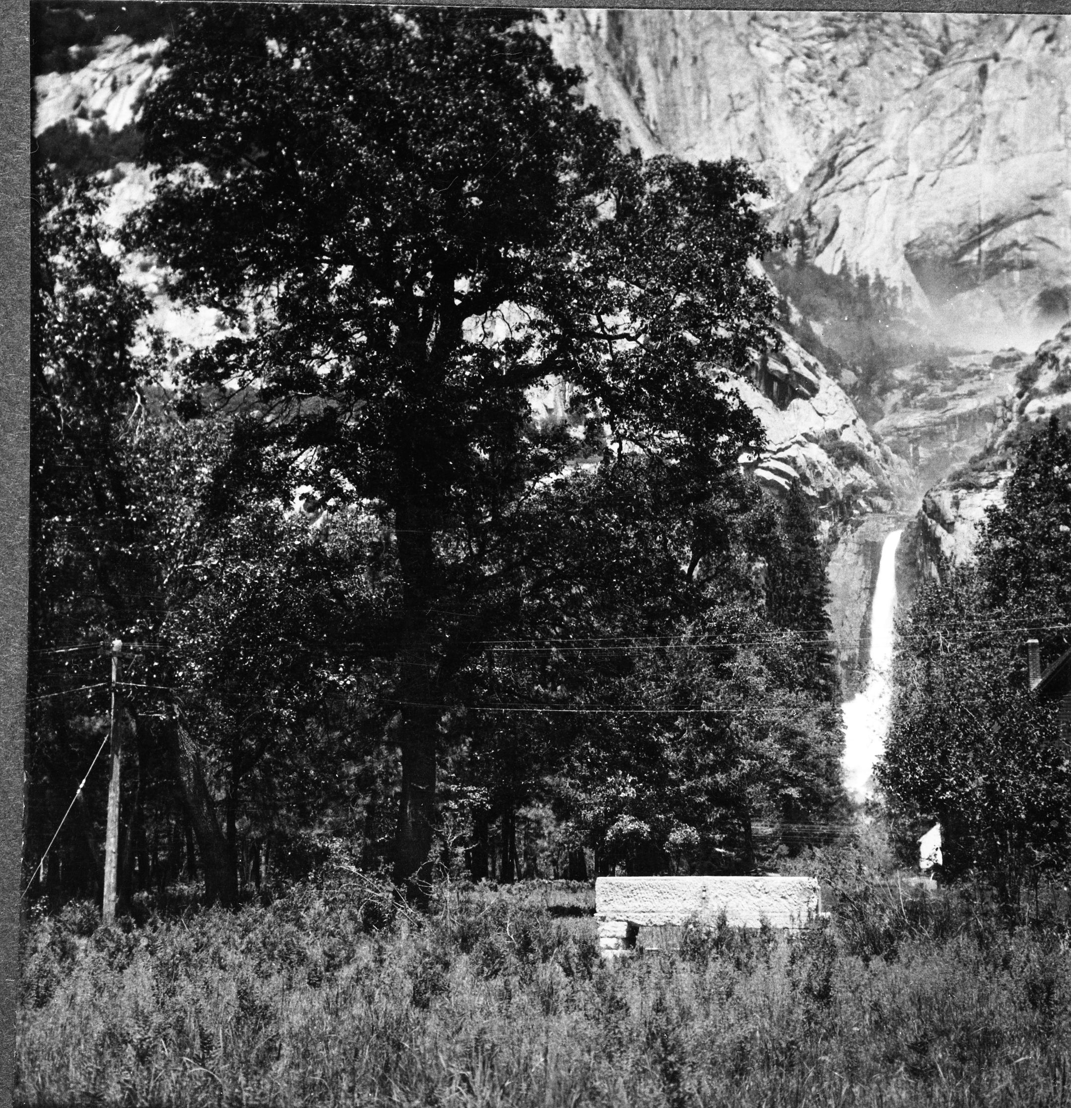 Copy Neg: 1985 by Michael Dixon. The Galen Clark memorial bench at the base of lower Yosemite Fall. The chimney & roof on the far right were probably part of the Y. P. & C. Co.'s maintenance yar. Full stereograph (RL-16,876). [Building was Sovulewski's home - Tim Snyder, February 10, 2003 - built 1910. Bench installed 1911 on south side of Northside Drive.]