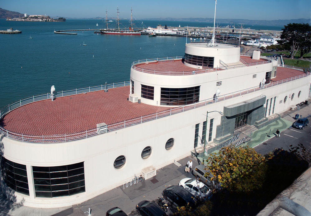 A building that is shaped like a ship with a red roof on the waterfront.