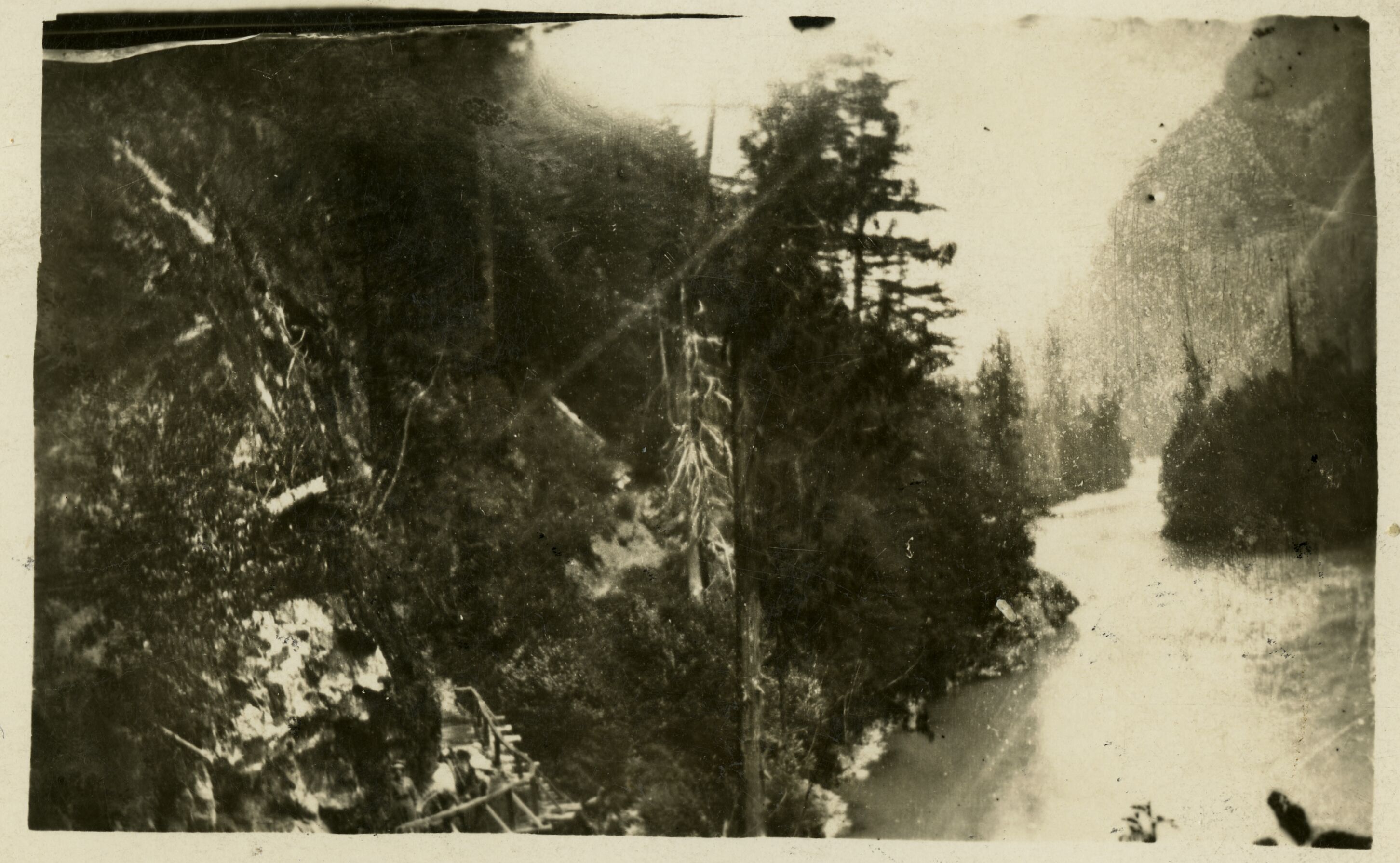 A river gorge thickly forested on either side.  A wooden trail is built along one rock face.