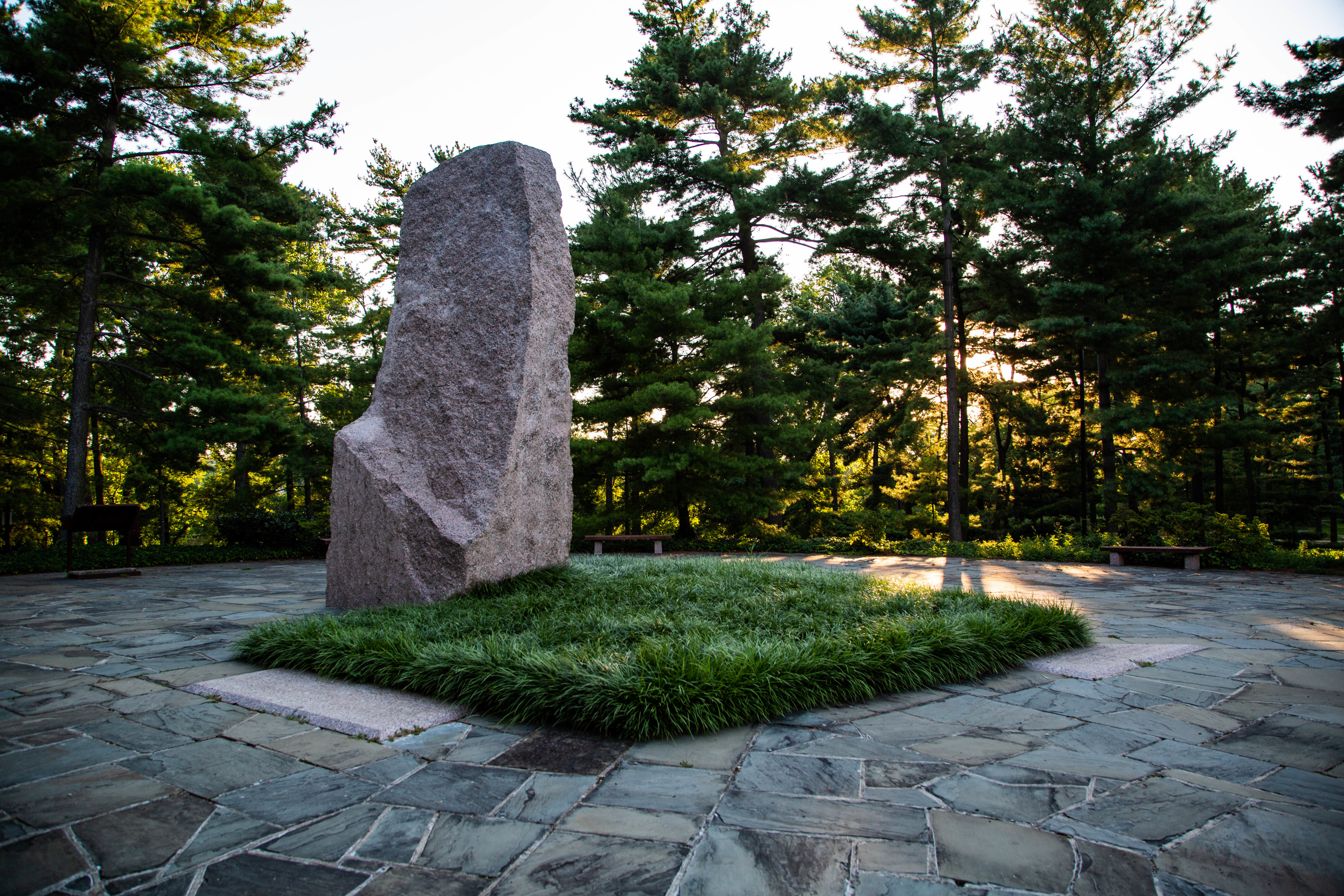 Granite monolith and grass patch on a stone plaza at sunset