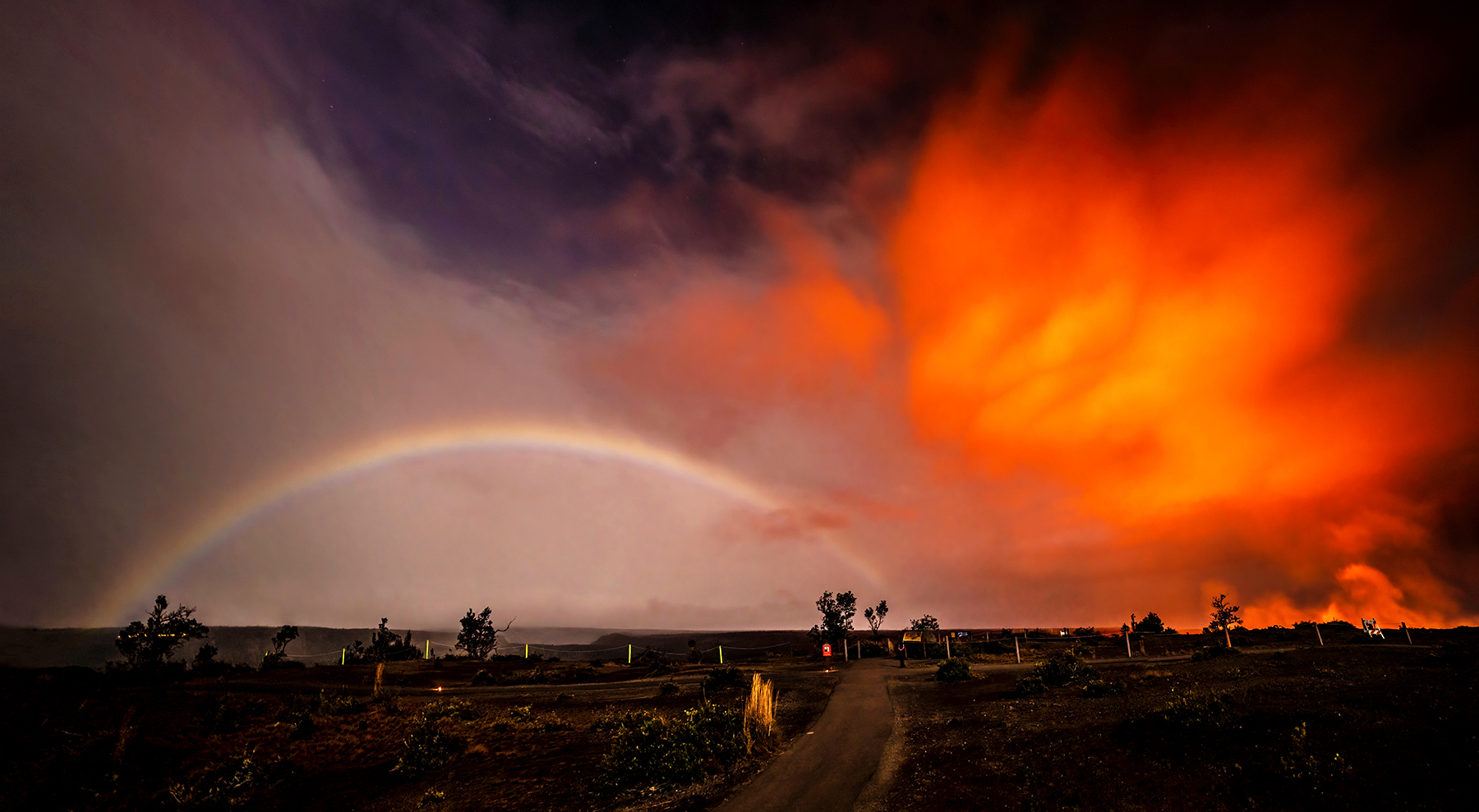 Trail towards caldera with a night glow from lava and a moonbow in the distance. 