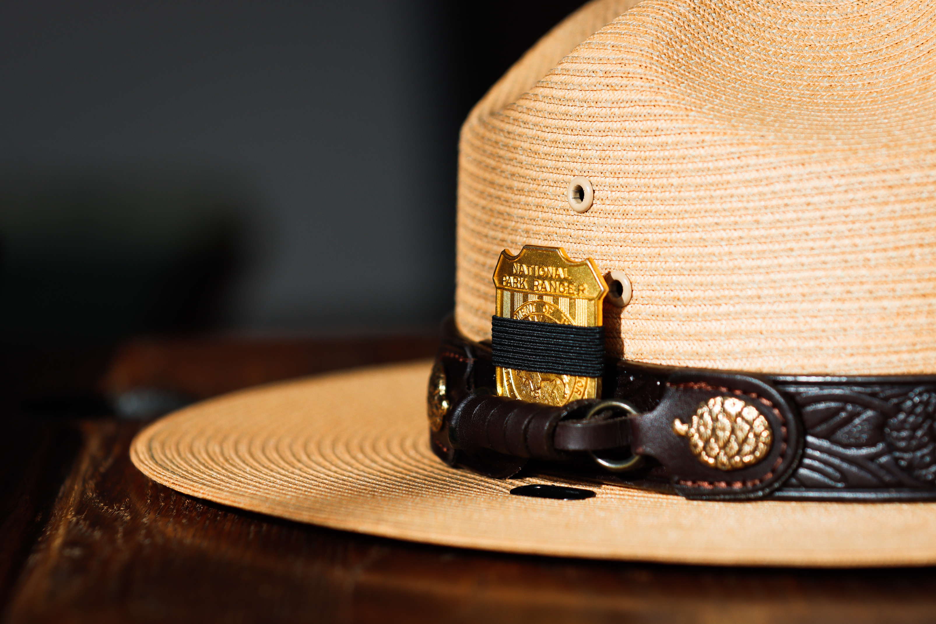 A Park Ranger's flat hat rests on a surface, prominently displaying the National Park Service badge on the front. A black mourning band wraps around the badge.