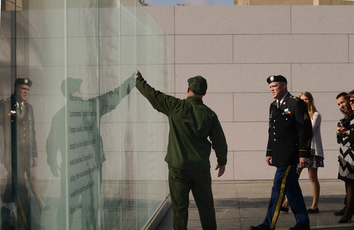 A ranger points to the glass wall memorial while talking to a man in military uniform