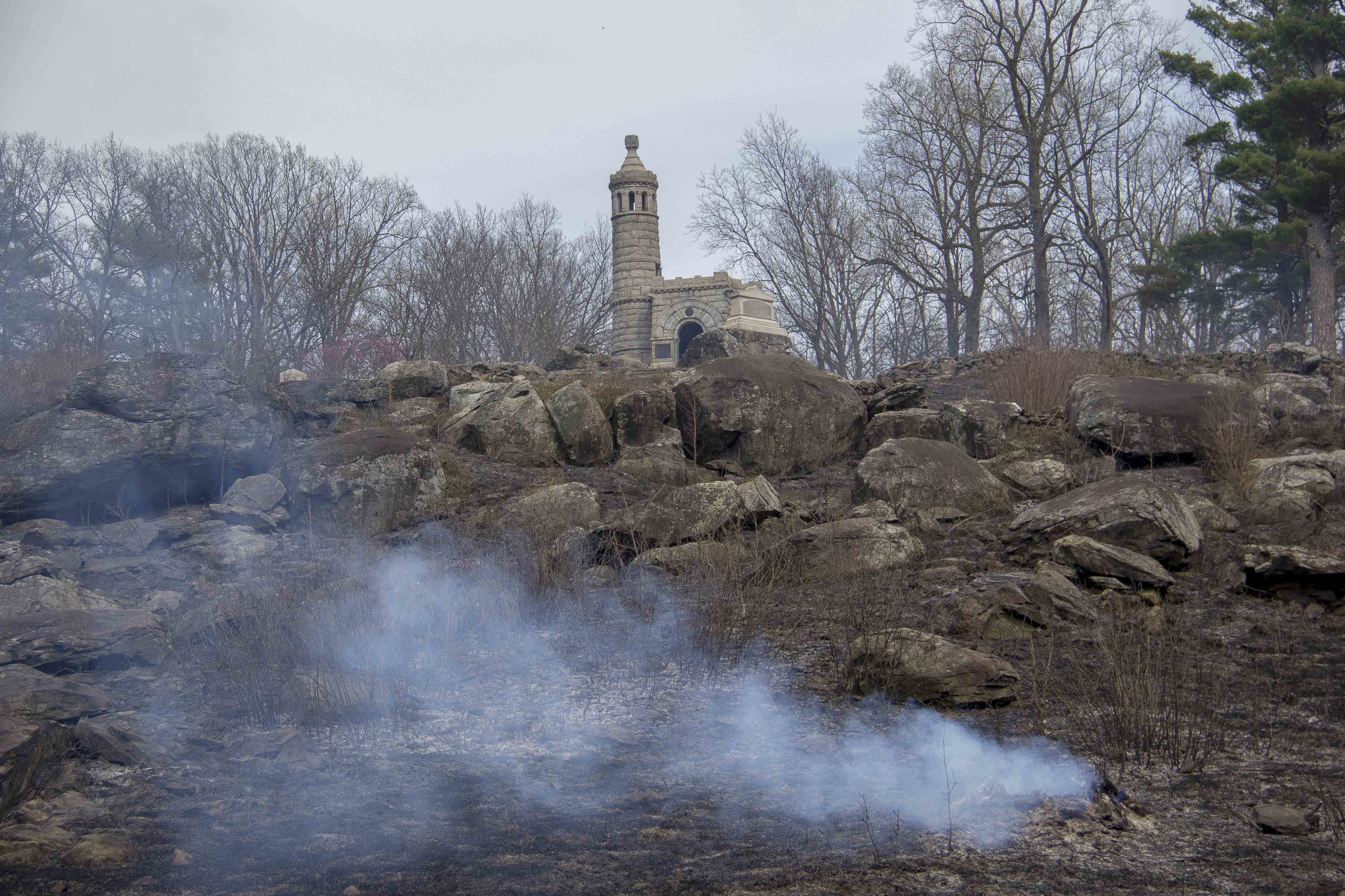 The prescribed fire has ended and only a few hot spots remain. There is a monument at the top of the hill while a small hot spot continues to smoke.