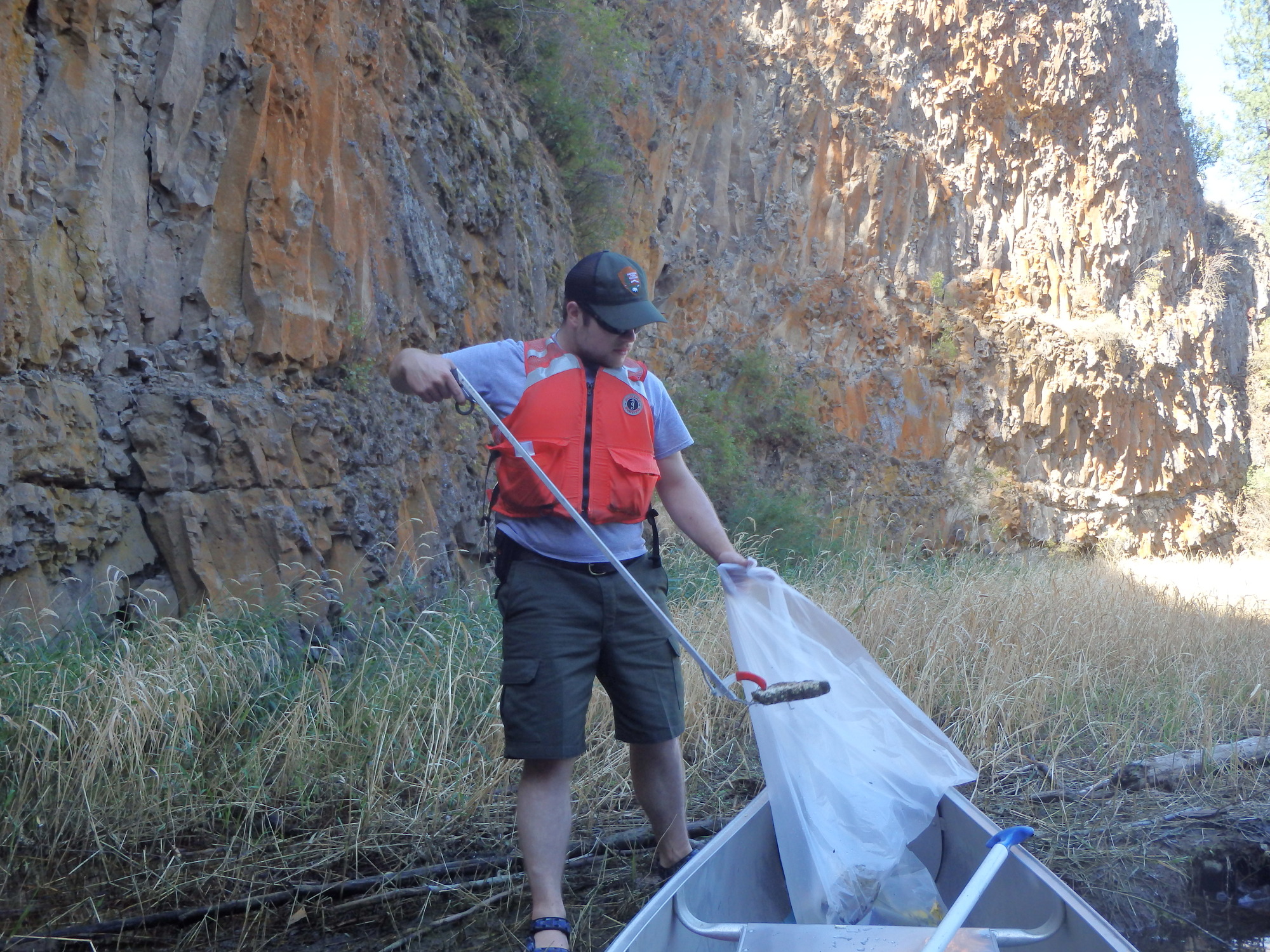 Color photograph of a ranger putting trash into plastic bag next to a canoe