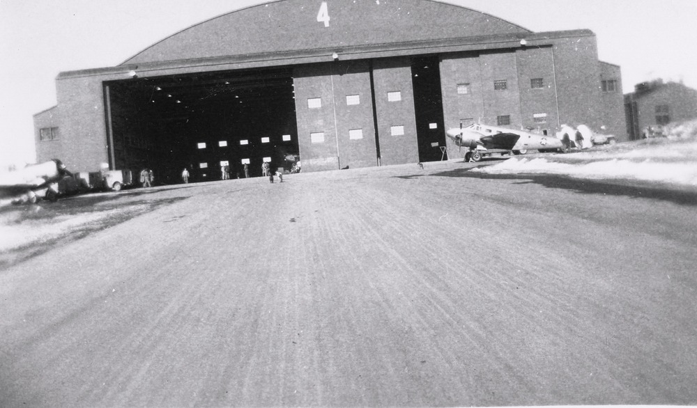 Large hanger building with people and planes nearby
