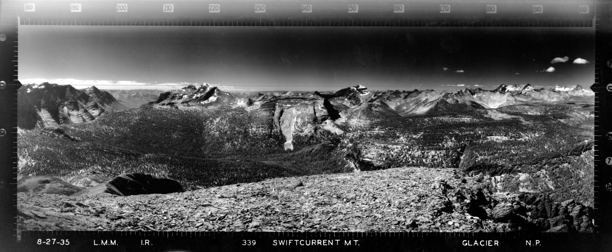 Infrared image of rocky outcropping with forested valley and craggy peaks in the distance.