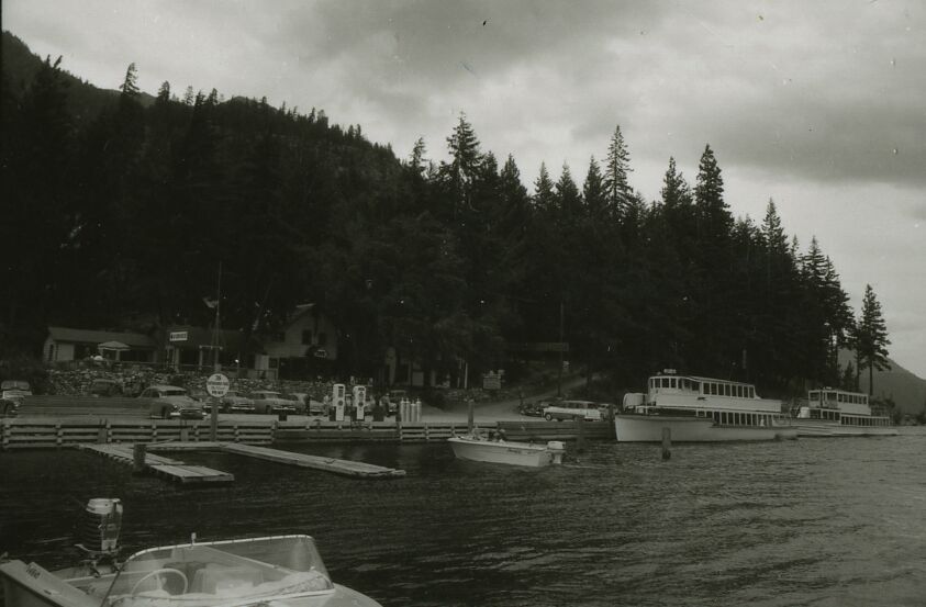A small town, docks, and boats on a lake, surrounded by forest.