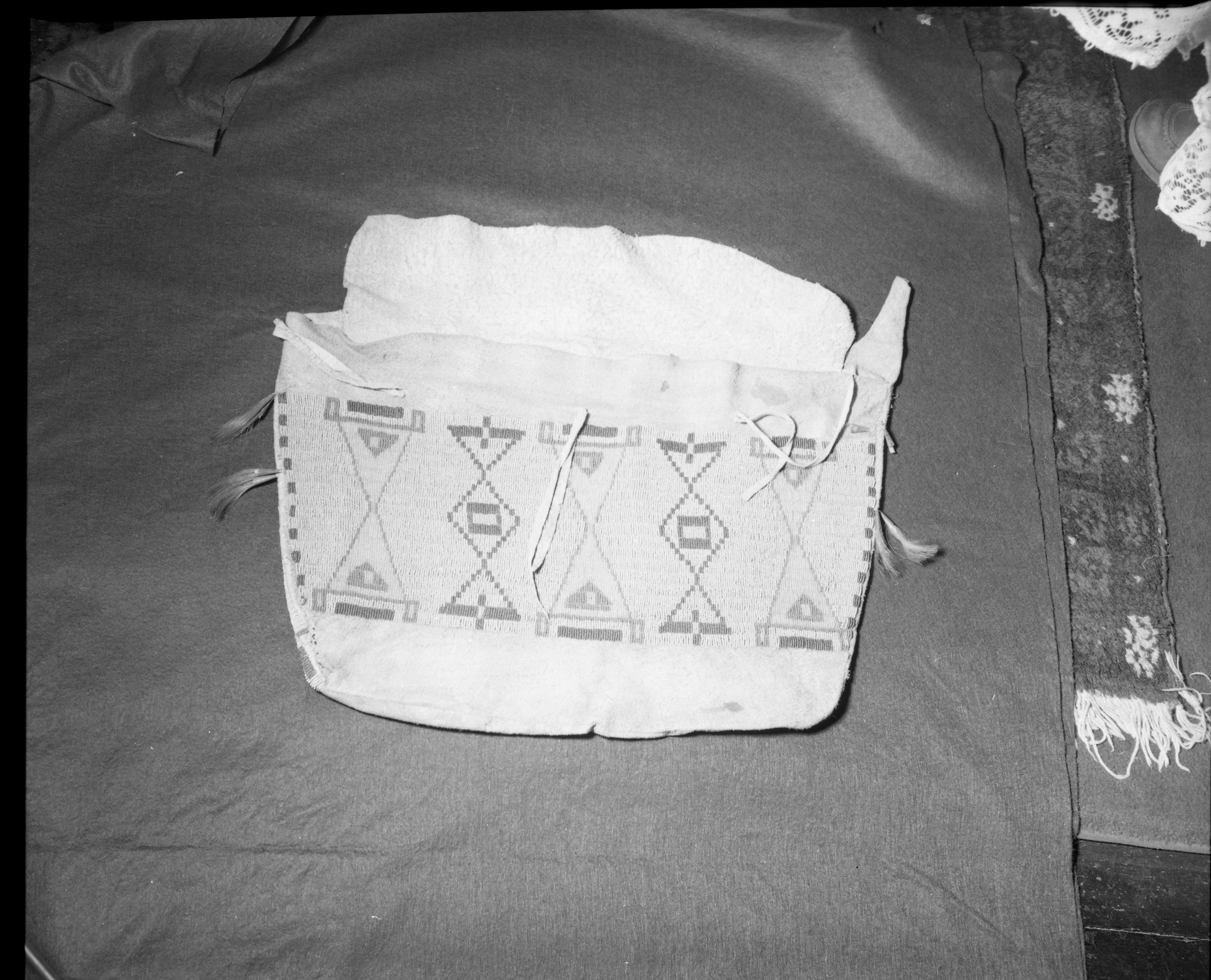 Mrs. Geraldine McConnell Collection. Object: Plains type beaded bag. Dimensions: Front - 22" x 13 1/2" Back - 18 1/2" x 18" wide at top and 16" wide at bottom. Side panels - 2 1/2" x 13 1/2" Bottom panel - 1 1/4" x 16 1/2". Technology & Materials: Brain tanned hide, sinew sewn with overcast stitch, turned right side out when completed. No welts used in seams. Beaded in lazy stitch in sinew using italian beads in opaque pink, dark blue, greasy yellow, turquoise, transparent clear, dark green, and medium blue. Three ties on body of sack with no matching holes on flap. In center top of front panel a 2" slit was made in the hide and sewn up with sinew, perhaps to take in excess hide. Brain tanned hide tabs project 5" from each side panel. Analine dyed horsehair emitting from tin cones completes decoration. Collection History: Purchased in a store in Mariposa, c. 1930's. Photographed by Michael Dixon January 1983. Catalogued by Craig Bates and Barbara Beroza. Yosemite collections, National Park Service.