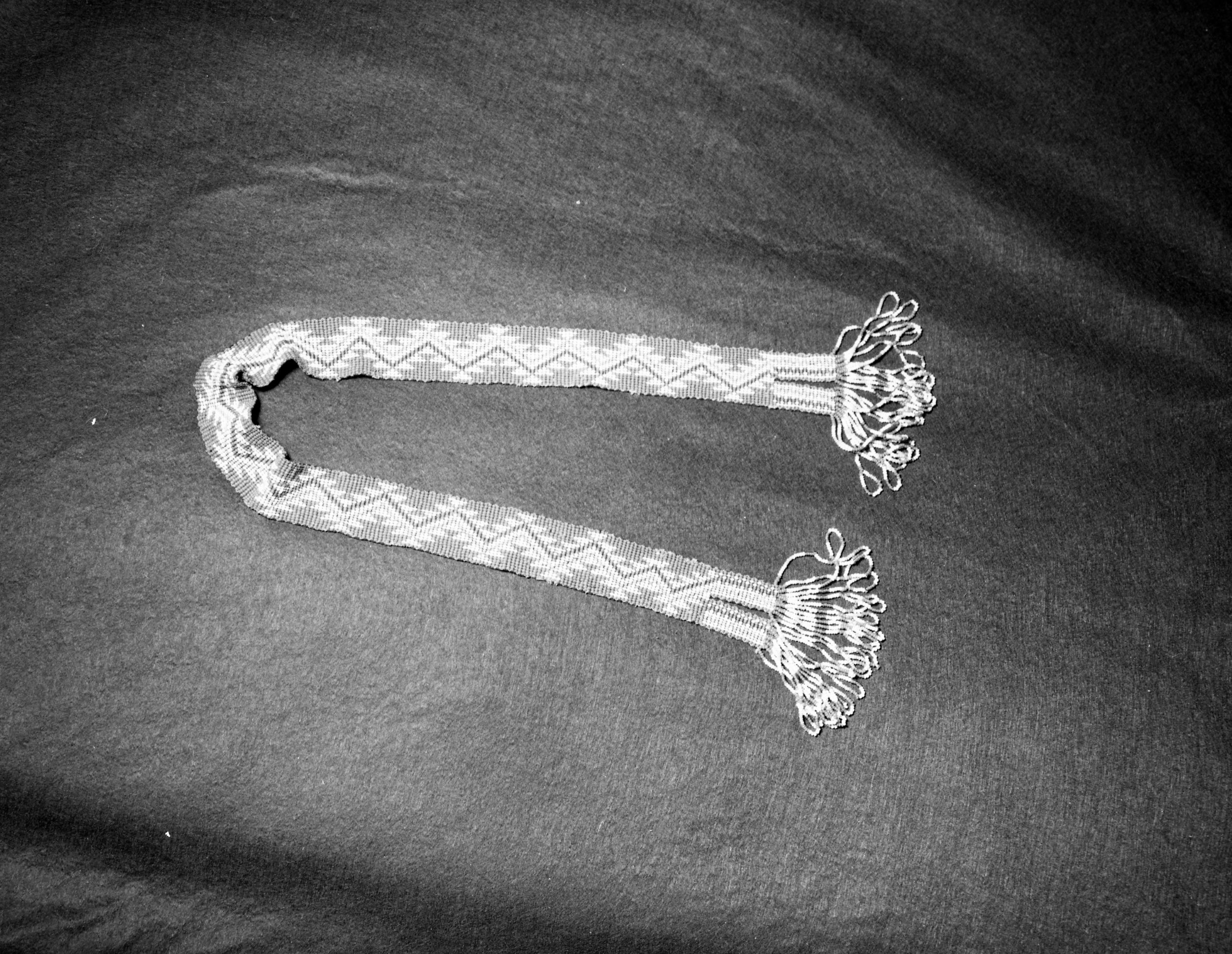 Mrs. Geraldine McConnell Collection. Object: Miwok beaded sash. Dimensions: 3.5 cm x 35". Materials: Commercial Thread, small 4/o Italian beads in brownish orange (background), medium blue, white, and white-centered rose. Technology: Single thread loomless beadwork, crossed wefts on edges, 23 beads wide. Collection History: Made by Calpine (Central Miwok of Sonora, died 1907 and buried in City Cemetery, Sonora) and acquired by a member of the Suggs Family of Sonora. Photographed by Michael Dixon in January 1983. Catalogued by Craig Bates and Barbara Beroza. Yosemite Collections, National Park Service.