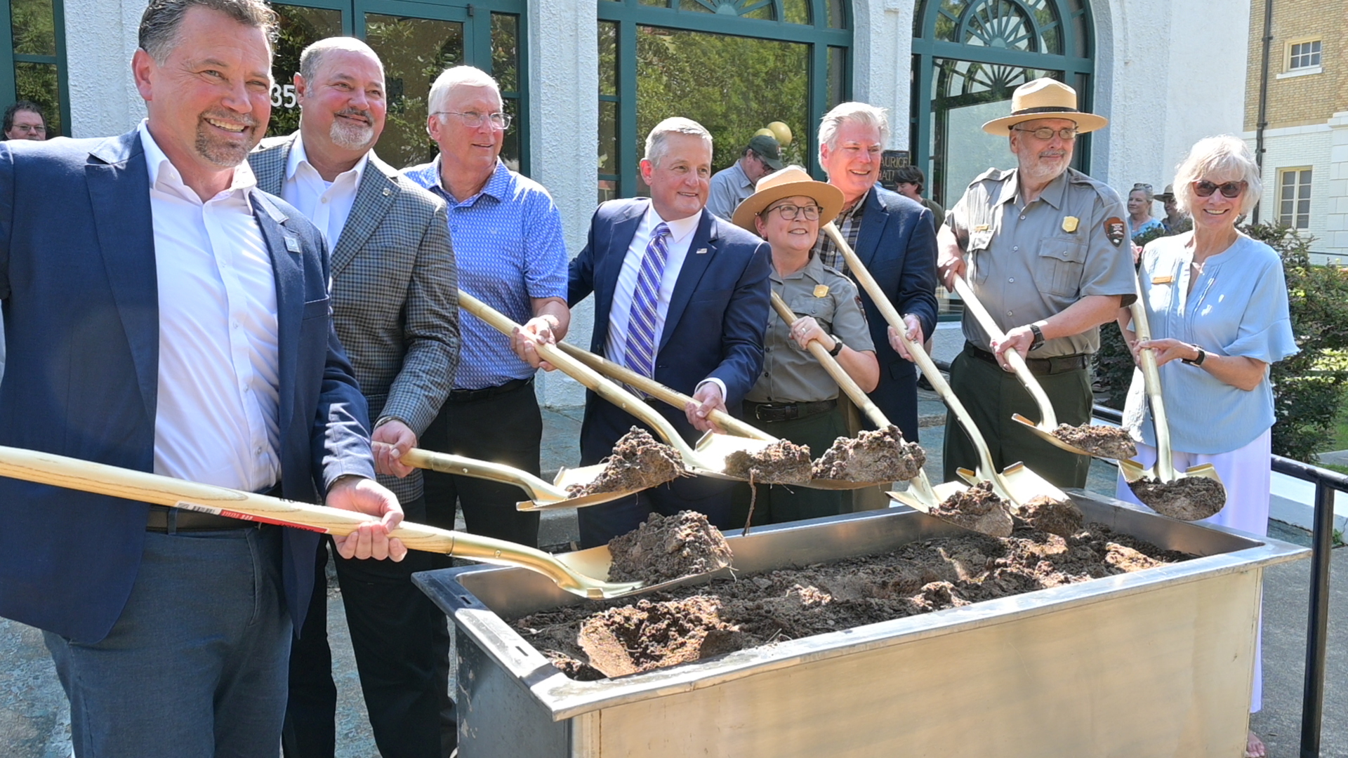 A group of people stand outside holding shovels filled with dirt