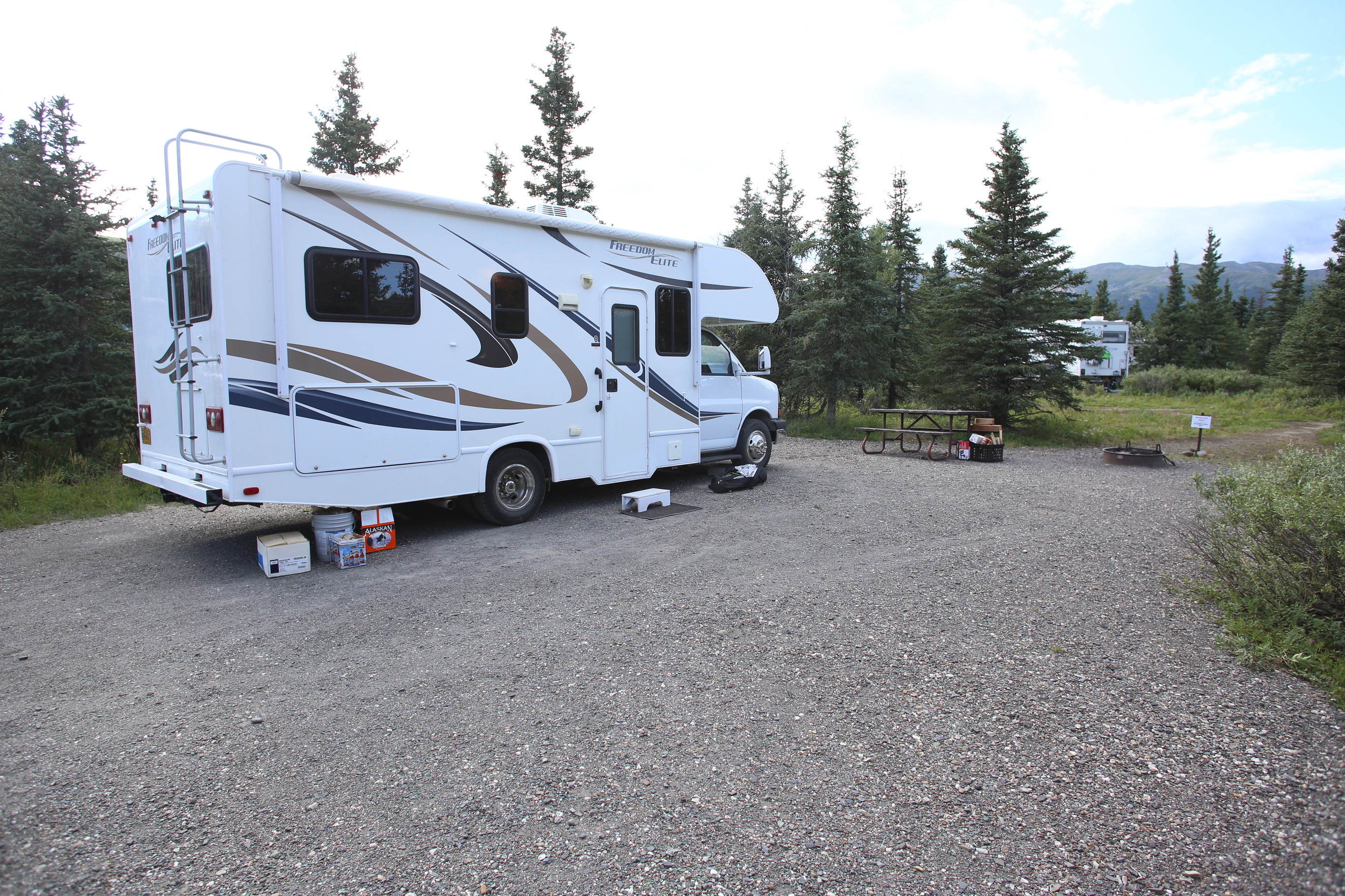 an R V parked on a gravel pad in a forest