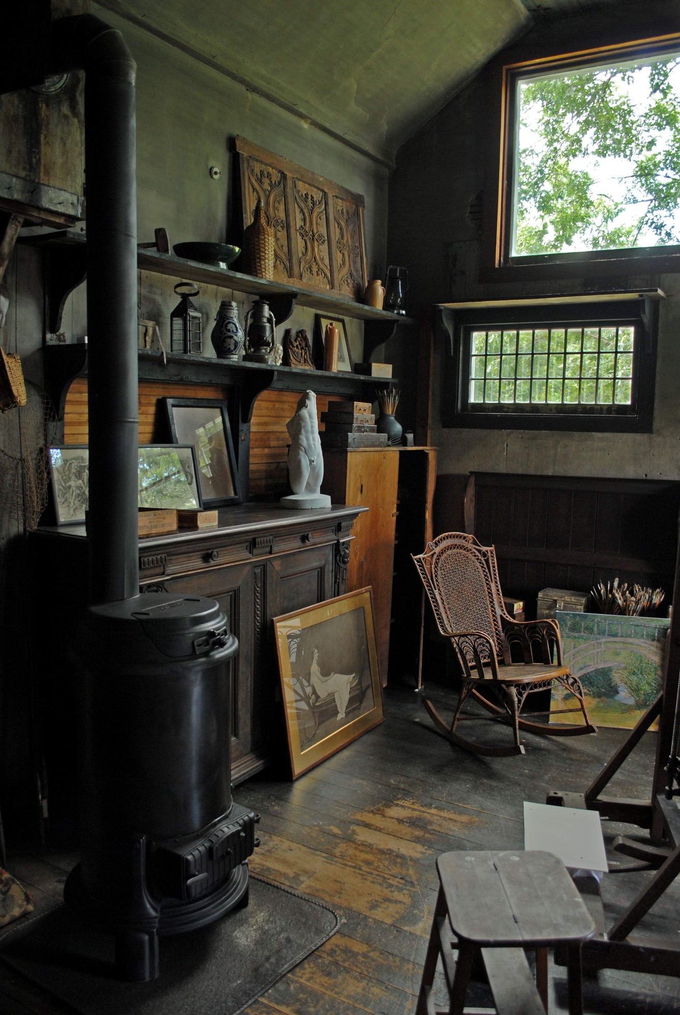A fireplace with several shelves filled with paintings and sculptures next to two large windows.
