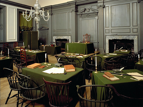 Tables and chairs are arranged in two semi-circular rows, facing a central table and chair.