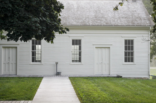 A light mist gives a white shine to the roof a broad white building and its freshly mown lawn.